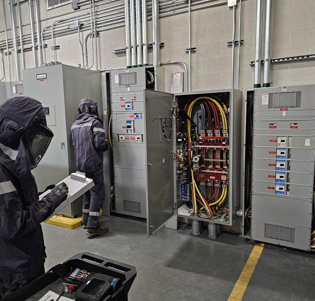 Amprite technicians in arc flash rated PPE working an energized switchgear lineup