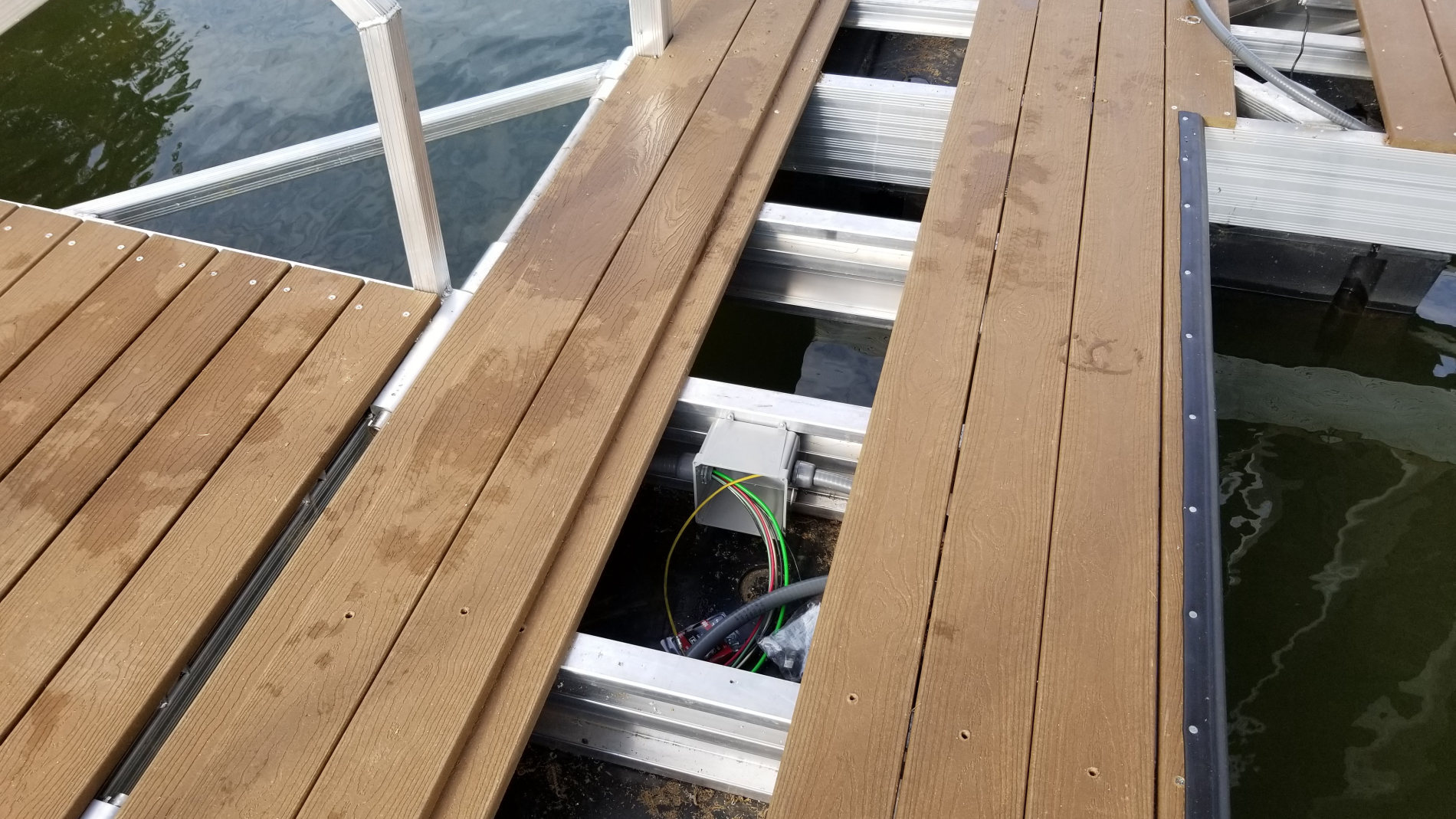 Dock junction box and wiring run beneath composite decking on a boat dock