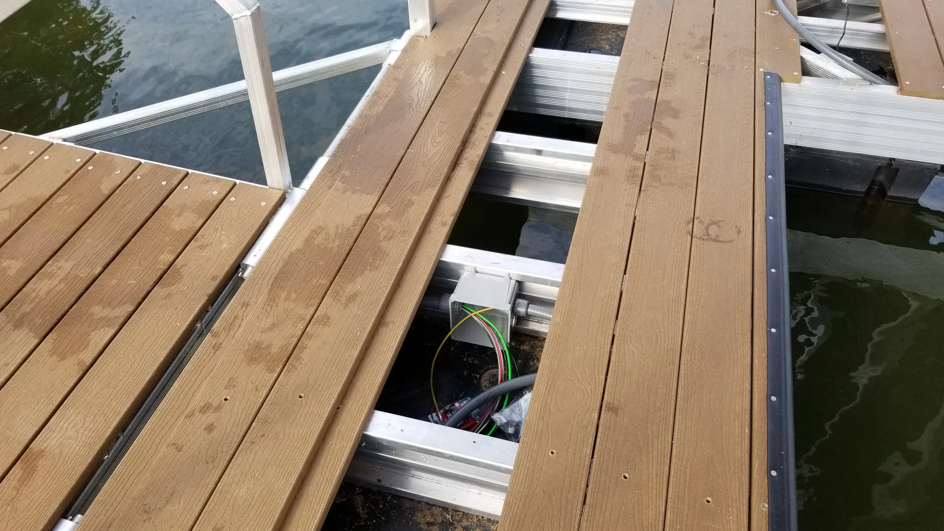 Dock junction box and wiring run beneath composite decking on a boat dock